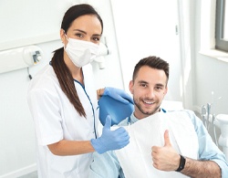 A younger man and his female dentist giving a thumbs up after undergoing a smile makeover