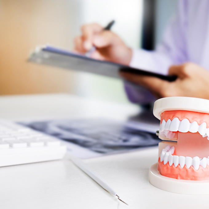 Dentures on desk with person writing on clipboard in background