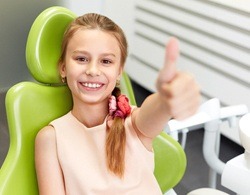 A young girl in the dentist chair giving a thumbs up during children's dentistry visit