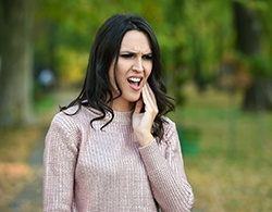 A young woman with long, dark hair holding her jaw in pain and needing to see an emergency dentist in Coatesville for her injury