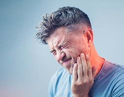 A middle-aged man holding his jaw and cringing in pain because of an abscess tooth