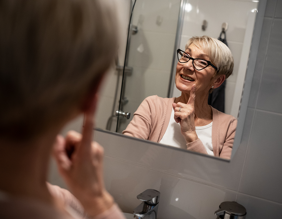 Older woman with glasses checking smile in mirror