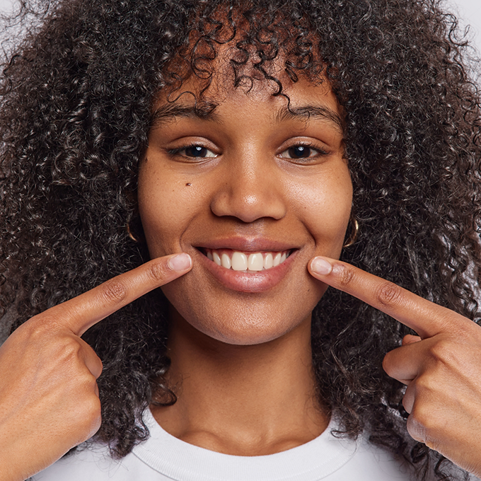 Woman with curly hair pointing to her teeth