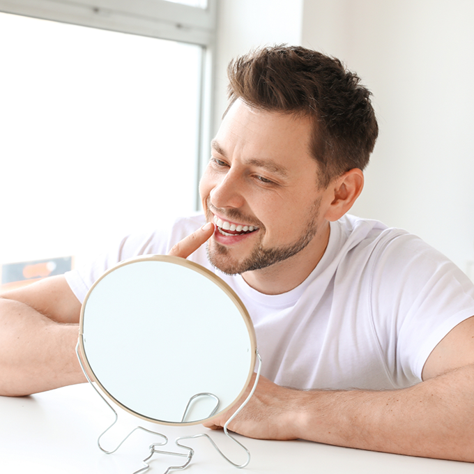 Man in white shirt checking tooth in mirror