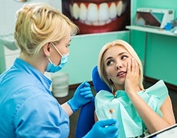 A young female holding her cheek while talking to her dentist about emergency dentistry