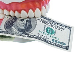 A mouth mold holding a $100 representing the cost of emergency dentistry