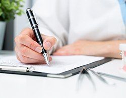 Dental professional writing information on a clipboard while dental instruments and a mouth mold sit nearby