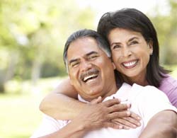 Couple with dental implant retained dentures outside smiling in Coatesville