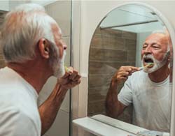 Man brushing his dental implant supported dentures in Coatesville