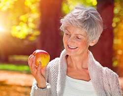 woman with dental implants in Coatesville holding an apple