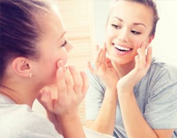 Young woman smiling in mirror after Invisalign teen treatment