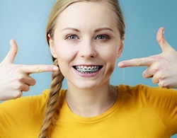 Young woman with braces pointing to her smile