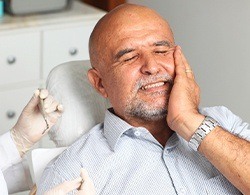Man in need of emergency dentistry for broken tooth holding cheek