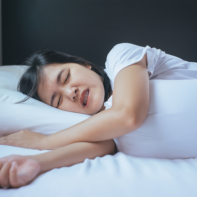 Young girl with braces lying in bed and grinding her teeth