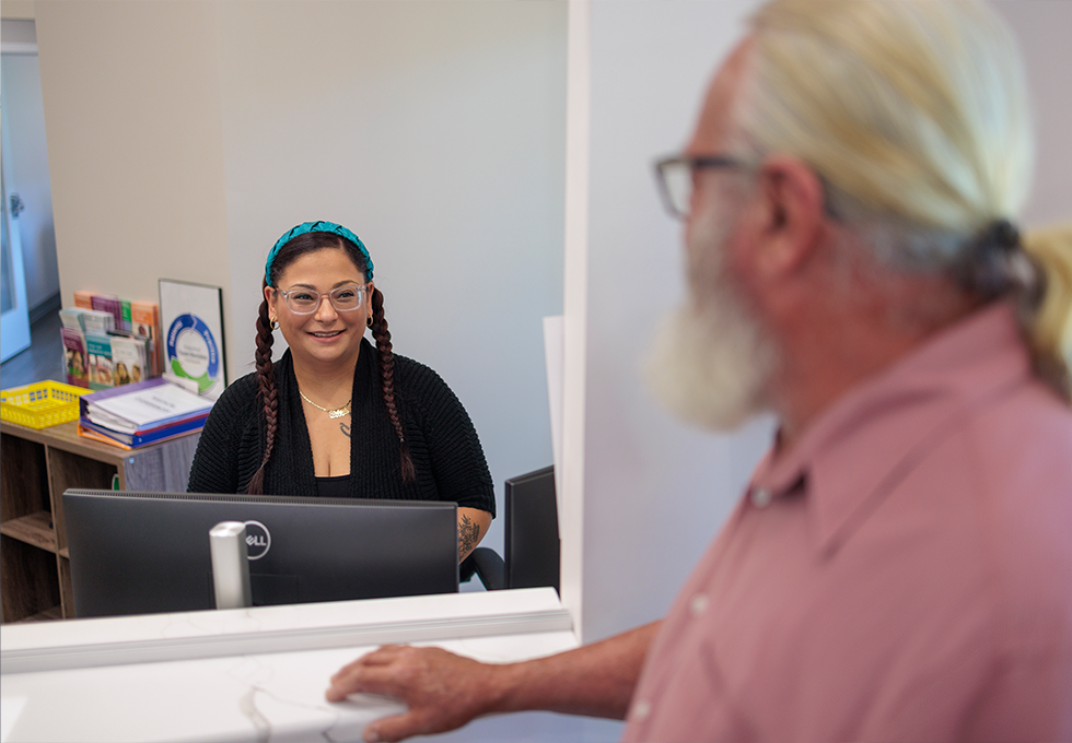 Female dental team member with glasses greeting male patient at front desk