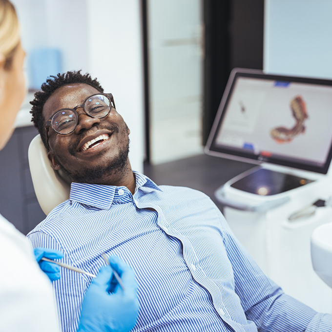 Man with glasses lying back in dental chair and smiling
