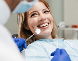 A young female under dental sedation smiling at her dentist while he prepares to check her teeth