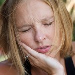 Woman with hand on her cheek in pain before emergency dentistry