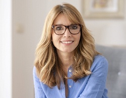 A middle-aged woman wearing glasses and seated on a couch and smiling after having a smile makeover in Coatesville