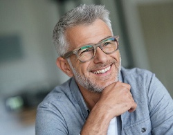 An older man wearing glasses and holding his chin and smiling