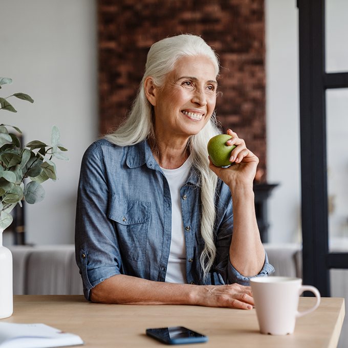 Smiling woman sitting at table and eating an apple