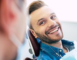 Man in denim shirt smiling at dentist during consultation