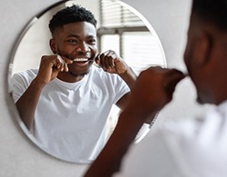 Man smiling while flossing his teeth in bathroom