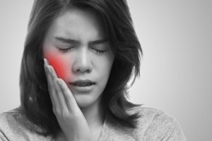 a young woman with braces holding her cheek in pain because of a dental emergency 