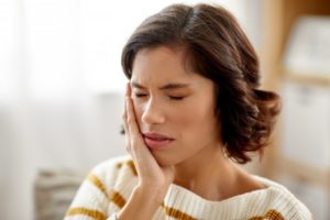 A young woman holding her cheek in pain while at home