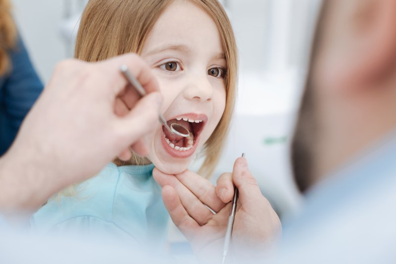 a little girl having her teeth and gums checked by a children’s dentist 