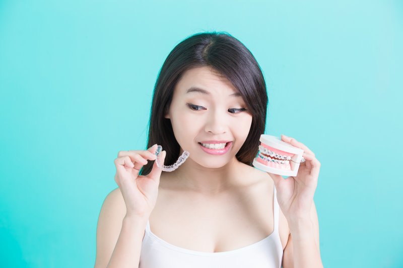 a young woman holds an Invisalign aligner and a mouth mold with traditional braces