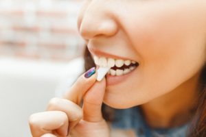 close up of a woman holding a  white piece of gum to her teeth