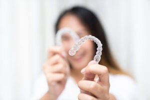 Woman smiling and holding up her Invisalign trays