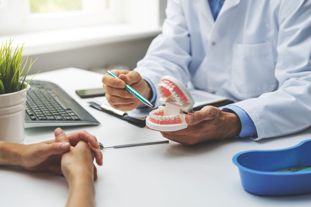 Hands of dentist and patient looking at model teeth at desk with keyboard