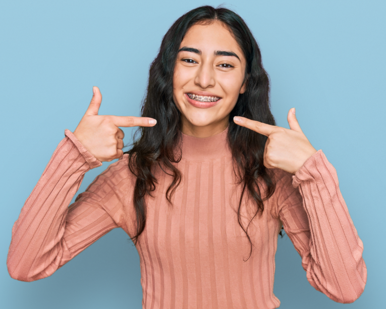 Girl with braces smiling and pointing at mouht
