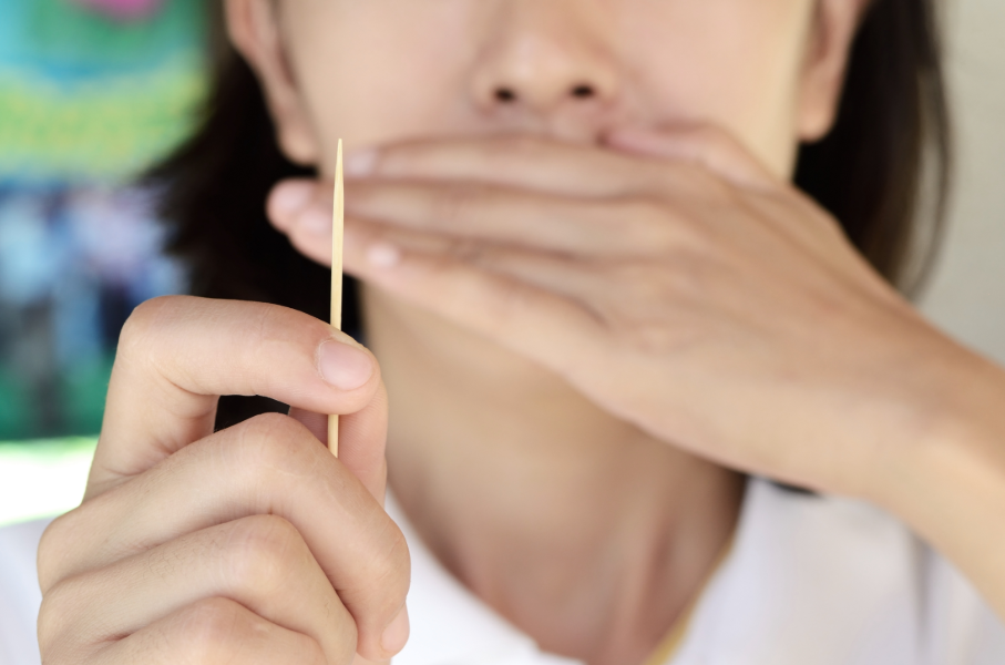 Woman holding toothpick and covering mouth