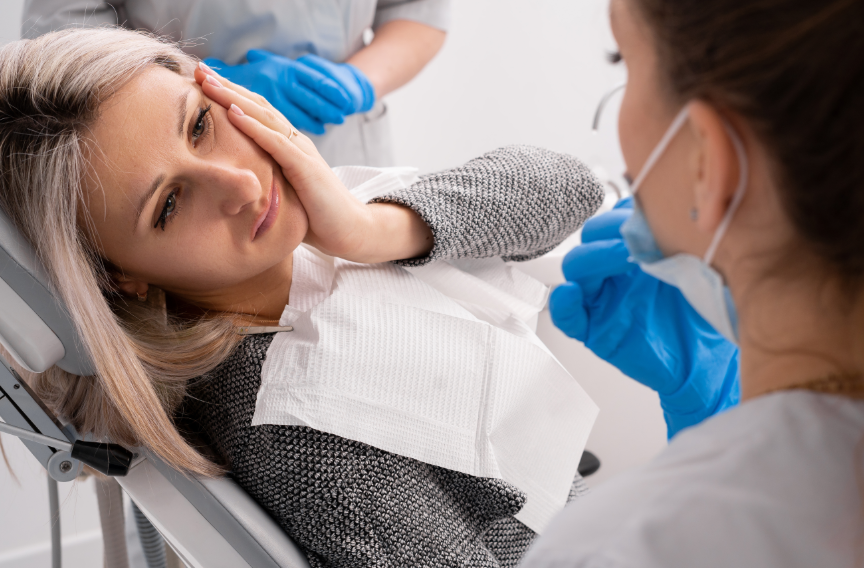 Patient in dental chair holding face, looking uncomfortable